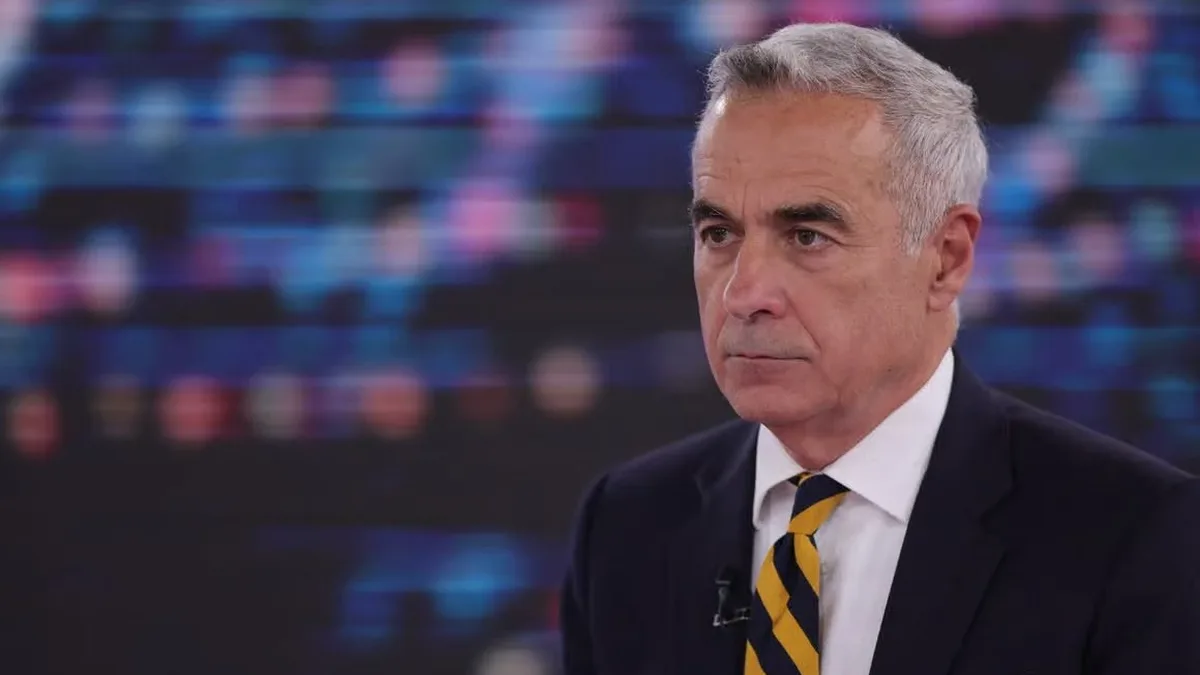 Călin Georgescu, în costum închis și cravată galbenă cu dungi bleumarin, într-un studio.