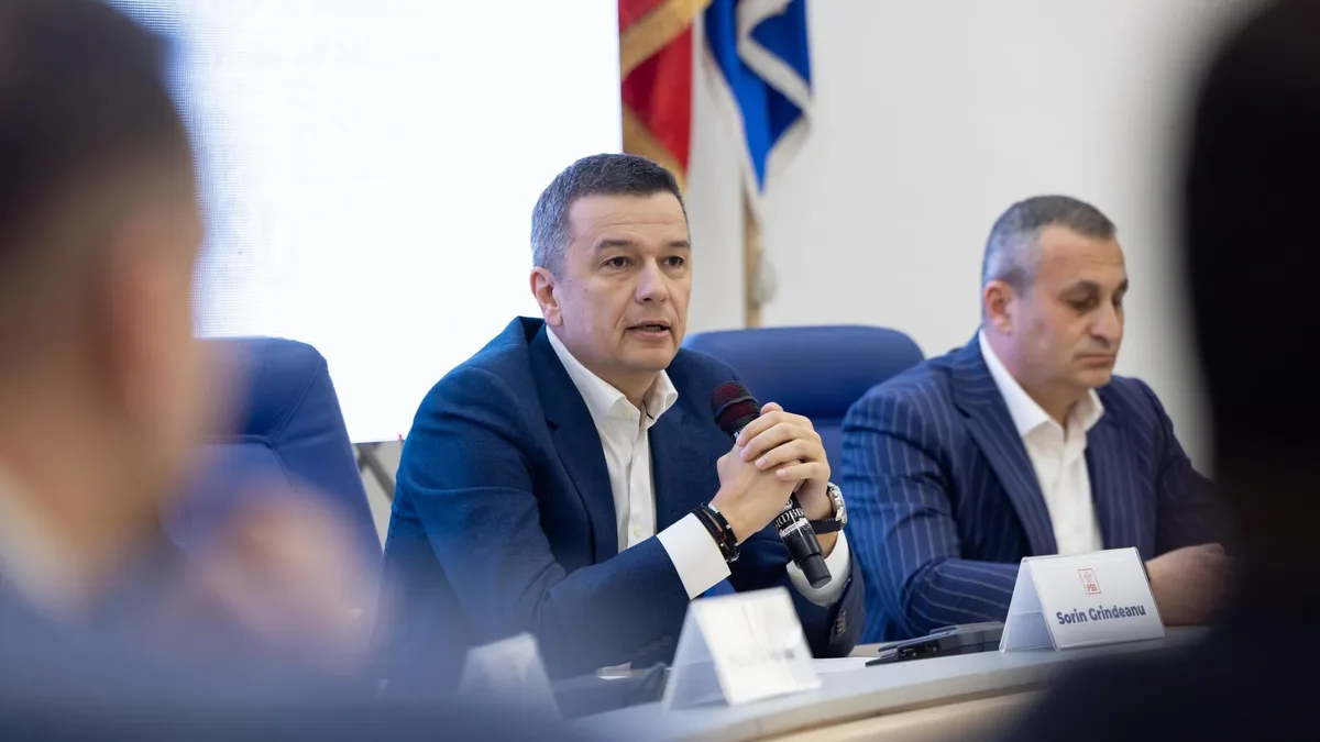 Sorin Grindeanu vorbește la un microfon, așezat la o masă, lângă un alt participant.