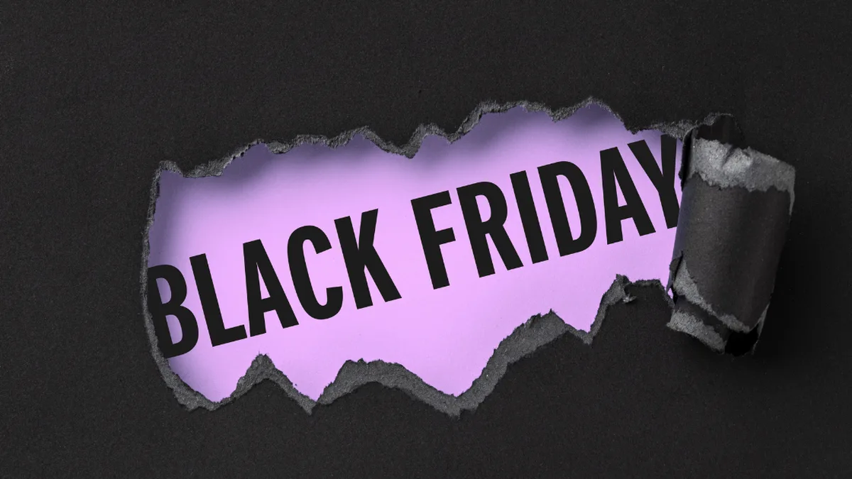 Textul „BLACK FRIDAY” pe un fundal mov, vizibil printr-o deschizătură cu margini rupte în hârtie neagră.