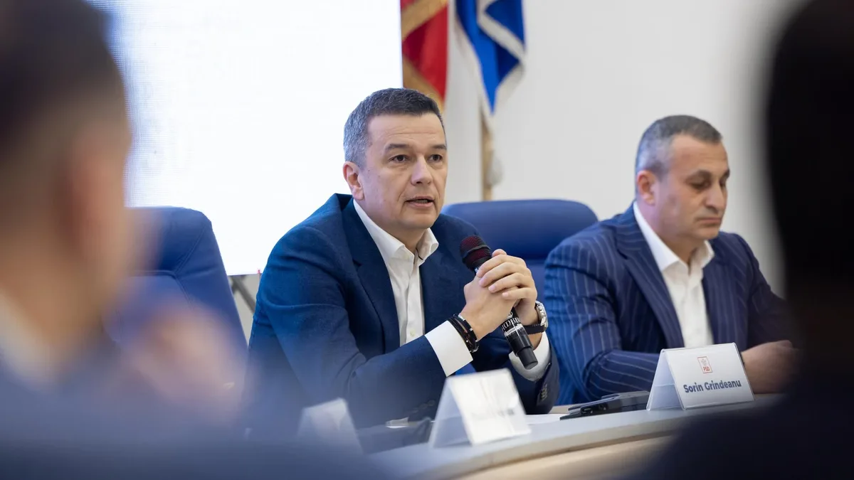 Sorin Grindeanu ține un microfon la o masă de reuniune, lângă un alt participant; în față se vede plăcuța cu numele său și sigla PSD.