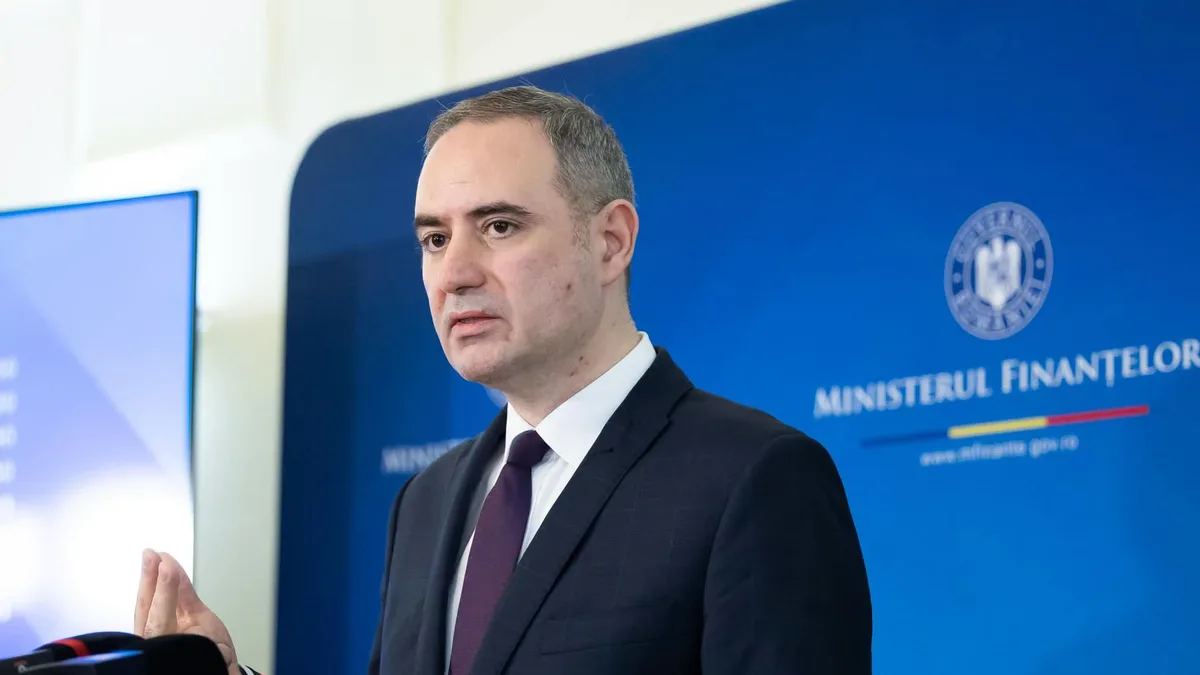 Alexandru Nazare vorbește la microfoane în fața unui panou al Ministerului Finanțelor.