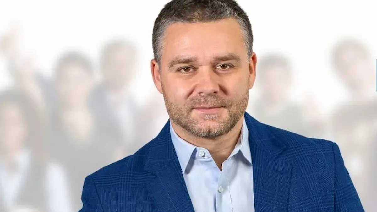 Ciprian Ciucu în sacou albastru și cămașă deschisă la culoare, pe un fundal luminos, estompat.