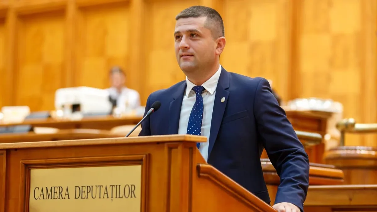 Radu Miruță la tribuna Camerei Deputaților, în fața unui microfon, într-o sală cu lambriuri din lemn.