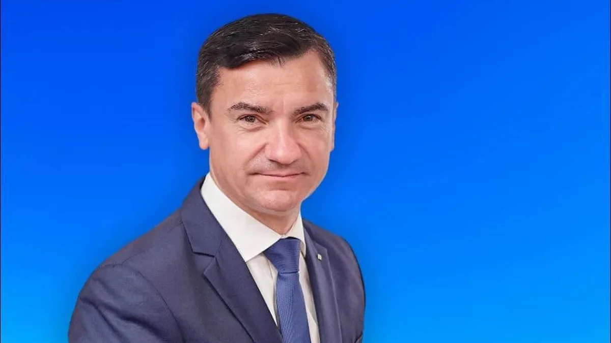 Mihai Chirica, în costum și cravată, cu mâinile împreunate, pe un fundal albastru.
