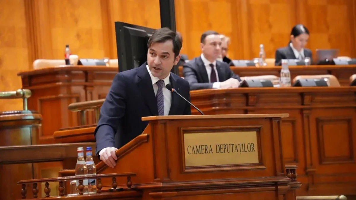 Sebastian Burduja vorbește la tribuna inscripționată „Camera Deputaților”, cu persoane așezate în fundal.