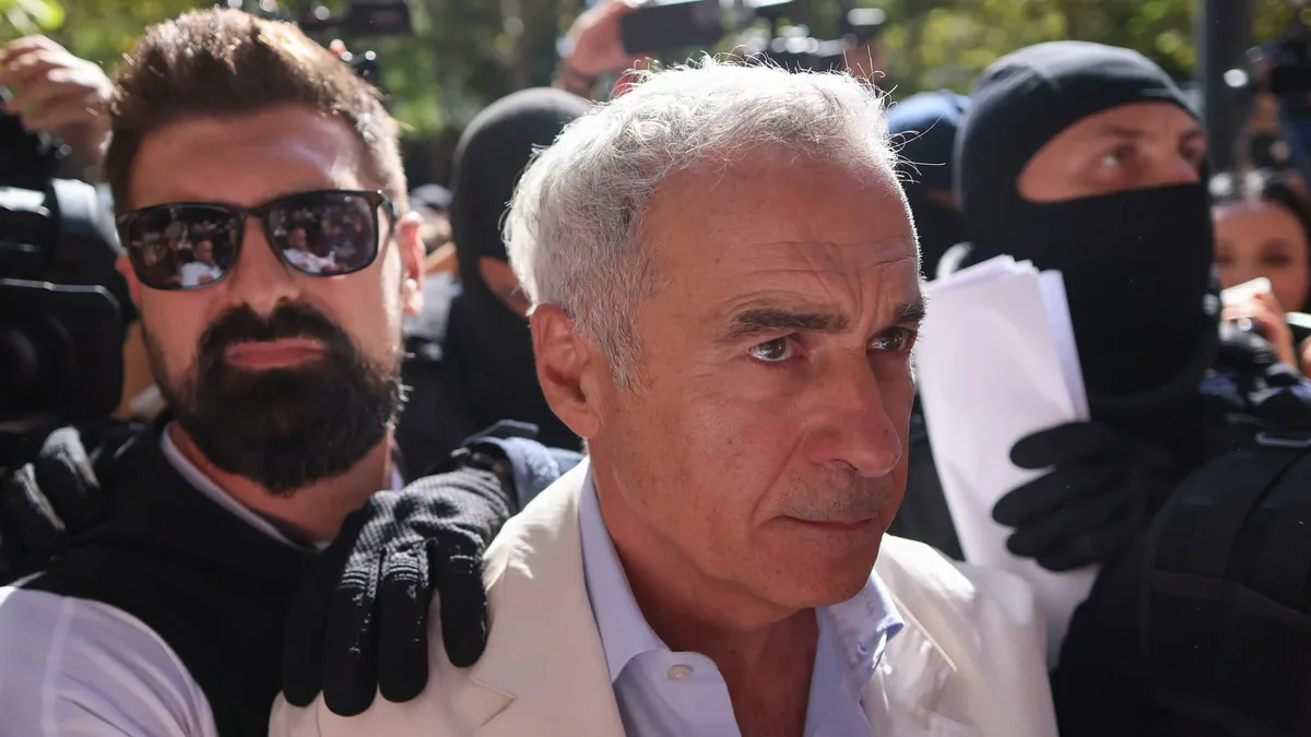 Călin Georgescu, în sacou deschis, înconjurat de persoane cu echipament tactic și camere de presă.