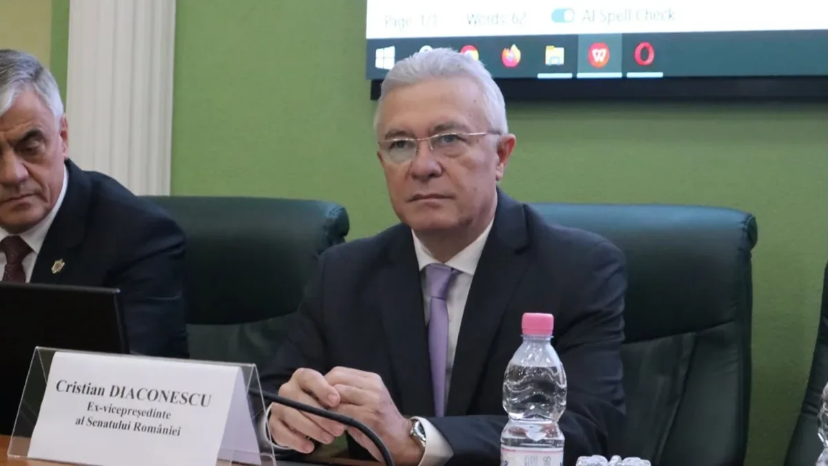 Cristian Diaconescu la o masă de reuniune, cu un microfon și un ecuson cu numele său în față.