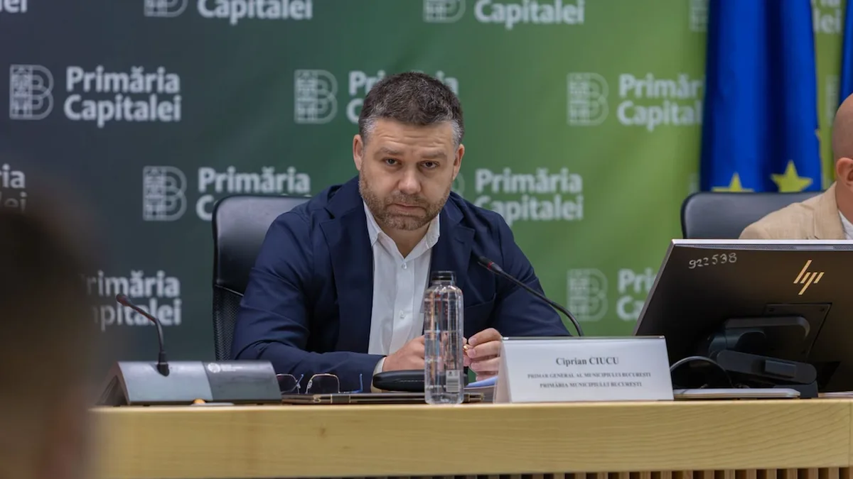Ciprian Ciucu la o masă cu microfon și plăcuță de identificare, în fața unui panou al Primăriei Capitalei.