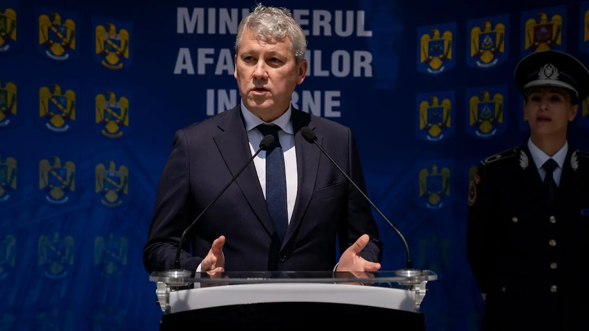 Cătălin Predoiu vorbește la un pupitru cu microfoane, în fața unui panou al Ministerului Afacerilor Interne.