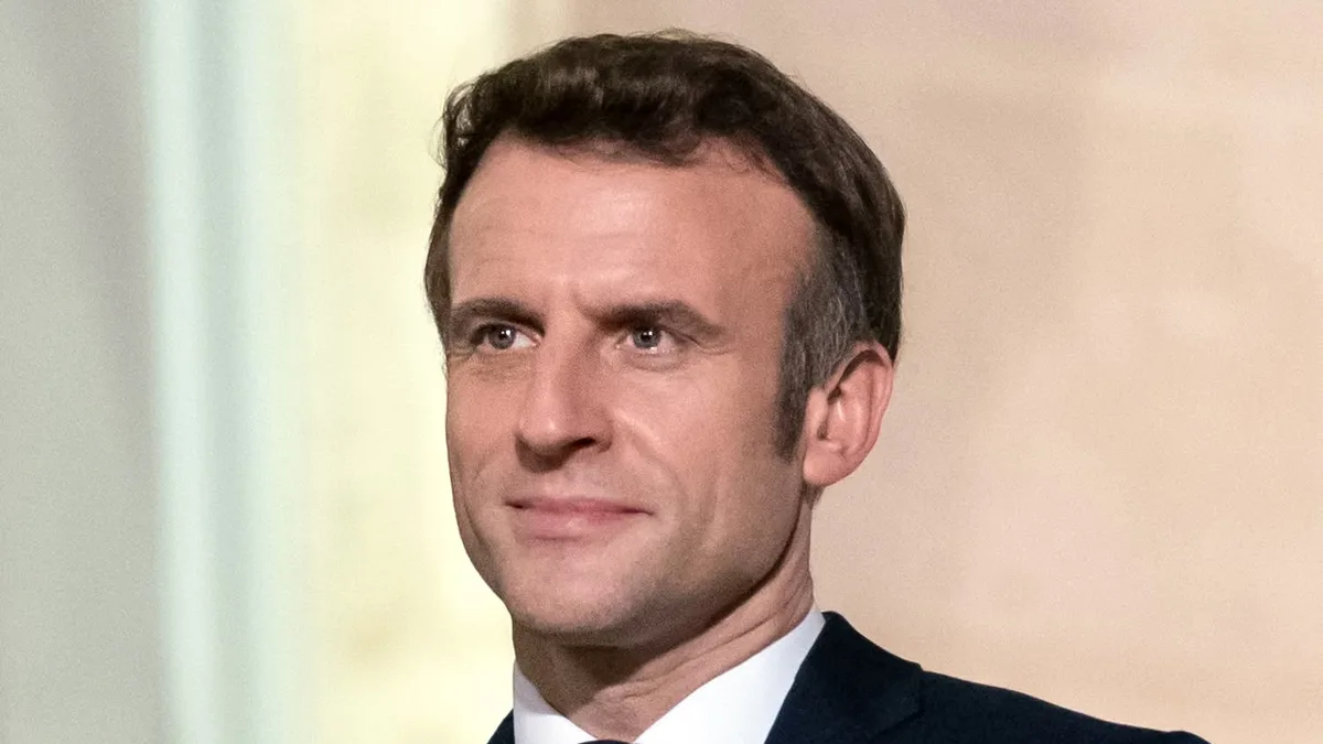 Emmanuel Macron, în costum închis și cravată, pe un fundal deschis și estompat.