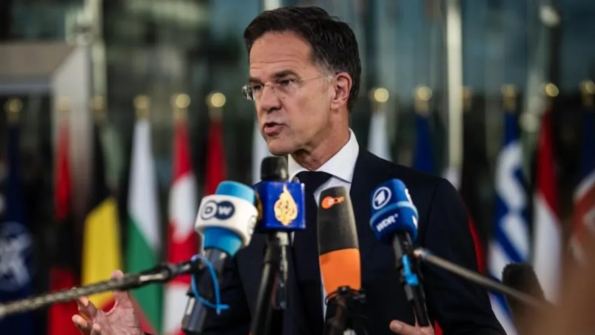 Mark Rutte vorbește la microfoane, cu drapele naționale și drapelul NATO în fundal.